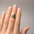 Hand wearing a ring with a green gemstone on a neutral background