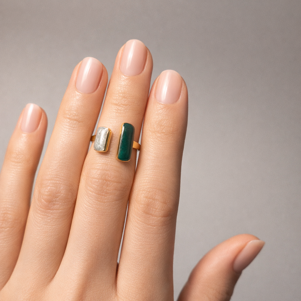 Hand wearing a ring with a green gemstone on a neutral background