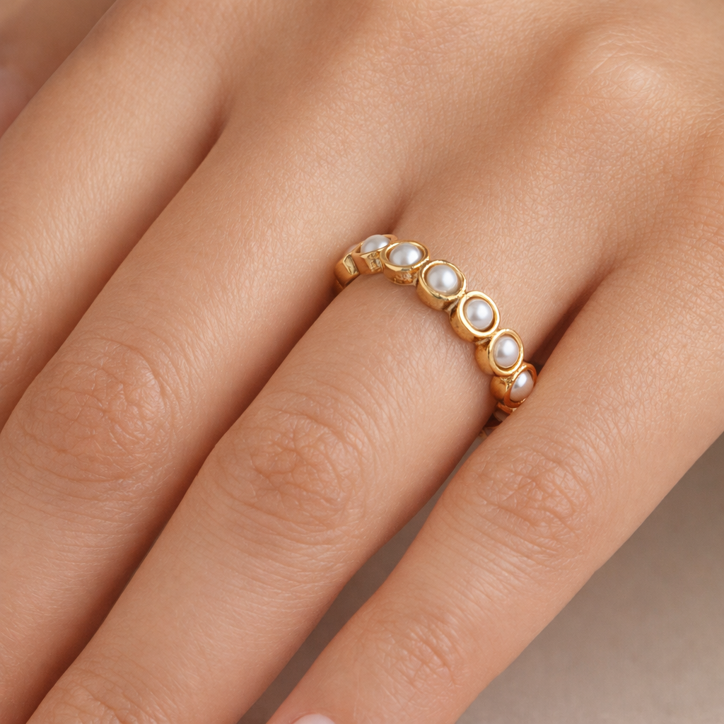 Gold ring with pearls on a hand against a neutral background
