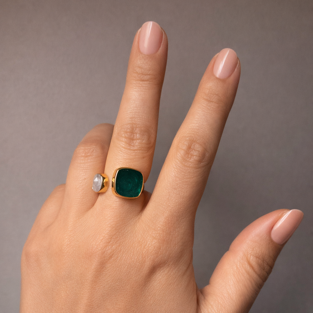 Hand wearing a green ring on a neutral background