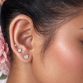 Close-up of an ear wearing two diamond stud earrings with a blurred background.