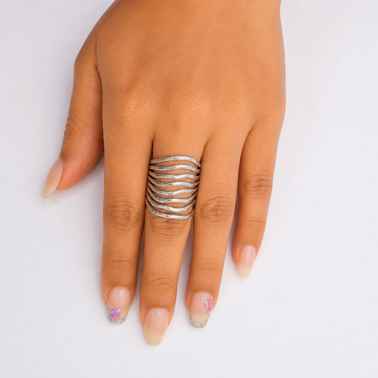A close-up of a hand wearing a wide silver ring with multiple wavy, parallel bands, set against a plain light gray background.