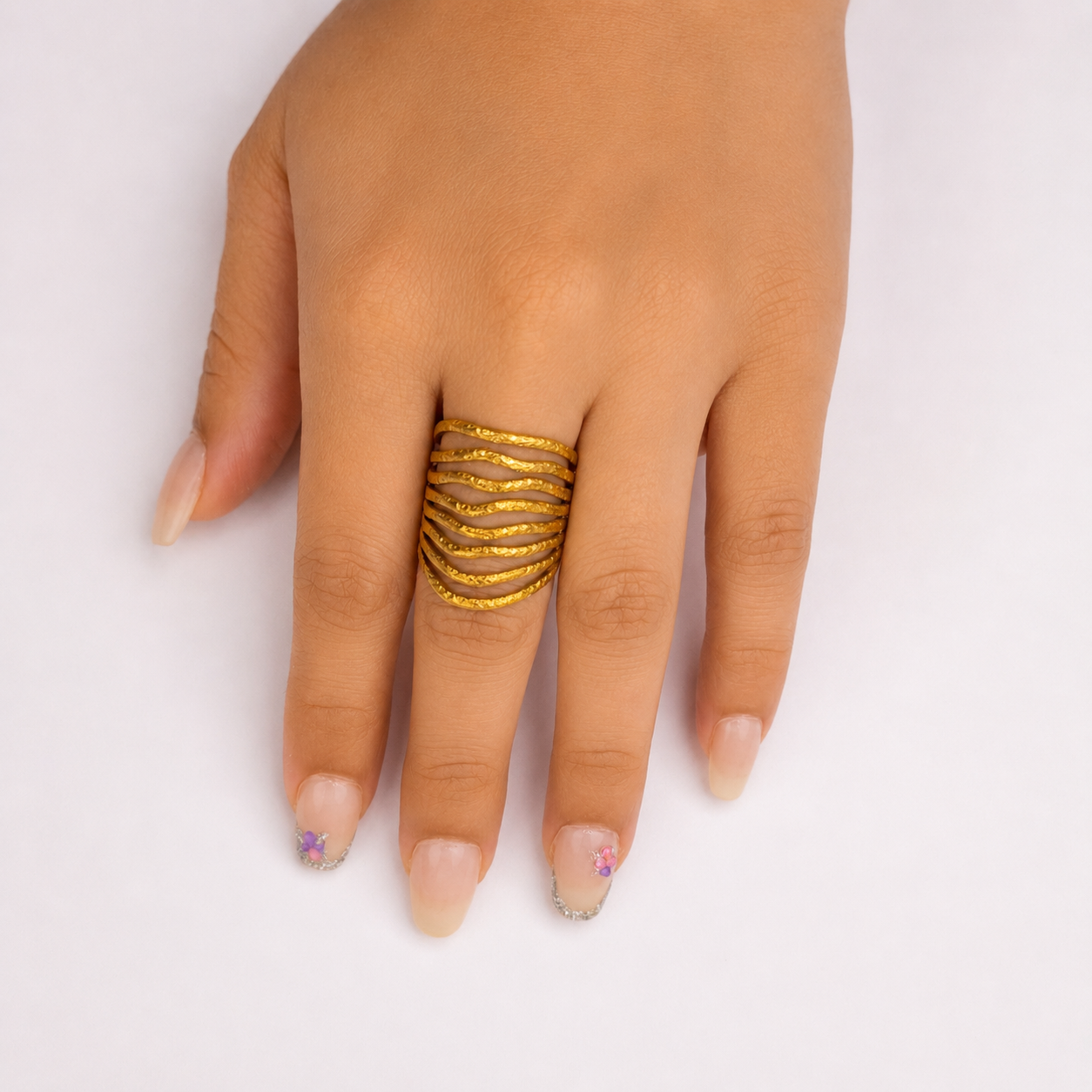 A close-up of a hand wearing a wide, multi-band gold ring on the middle finger, set against a plain white background.