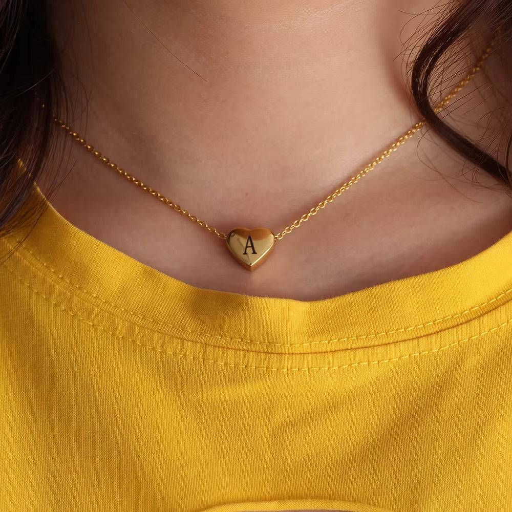 Gold necklace with a heart-shaped pendant featuring an 'A' on a yellow shirt.