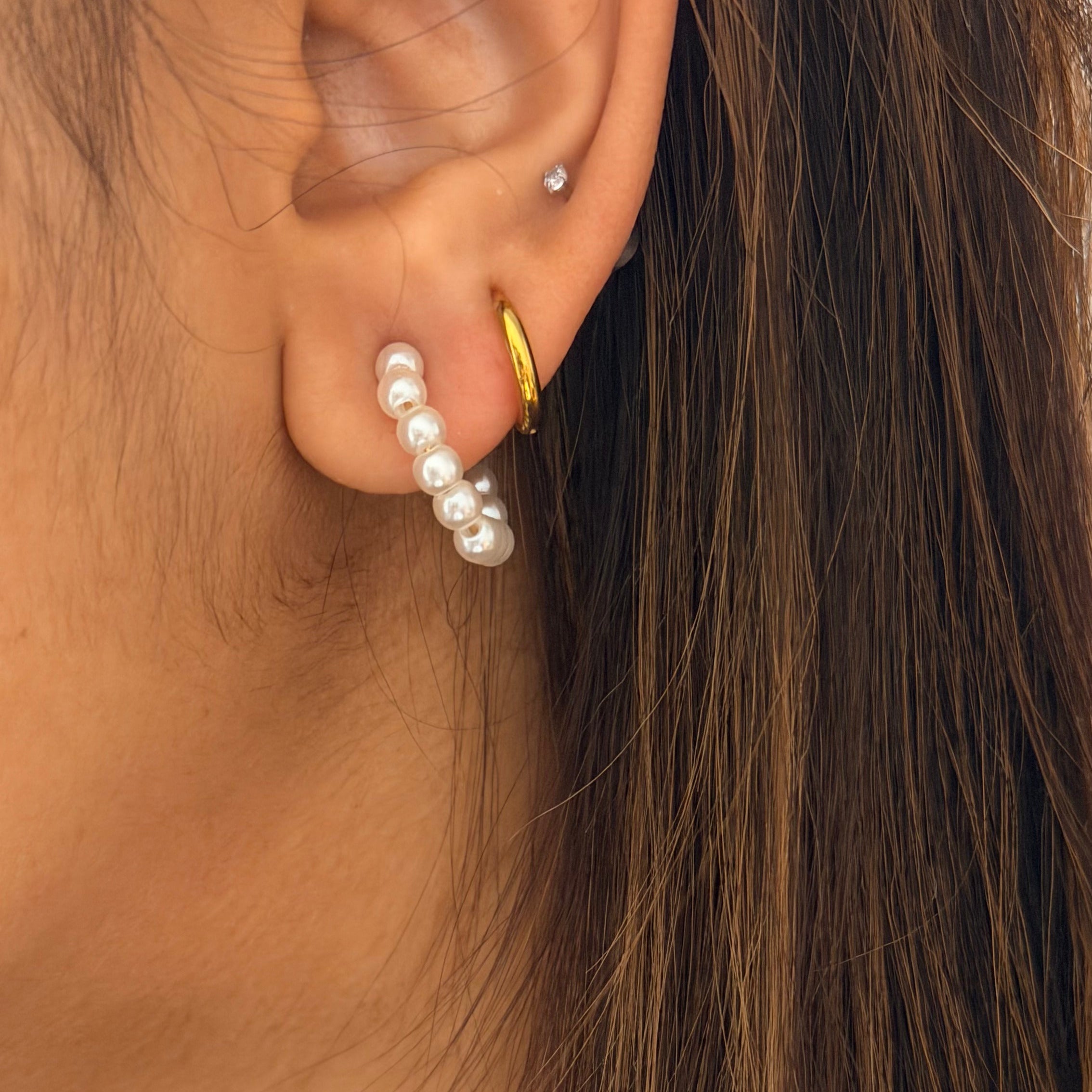 Close-up of an ear wearing a gold hoop earring and pearl stud earring.