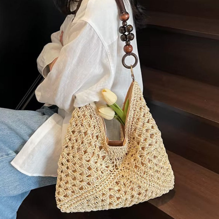 Person holding a woven handbag with wooden handle and beads, sitting on a wooden bench.