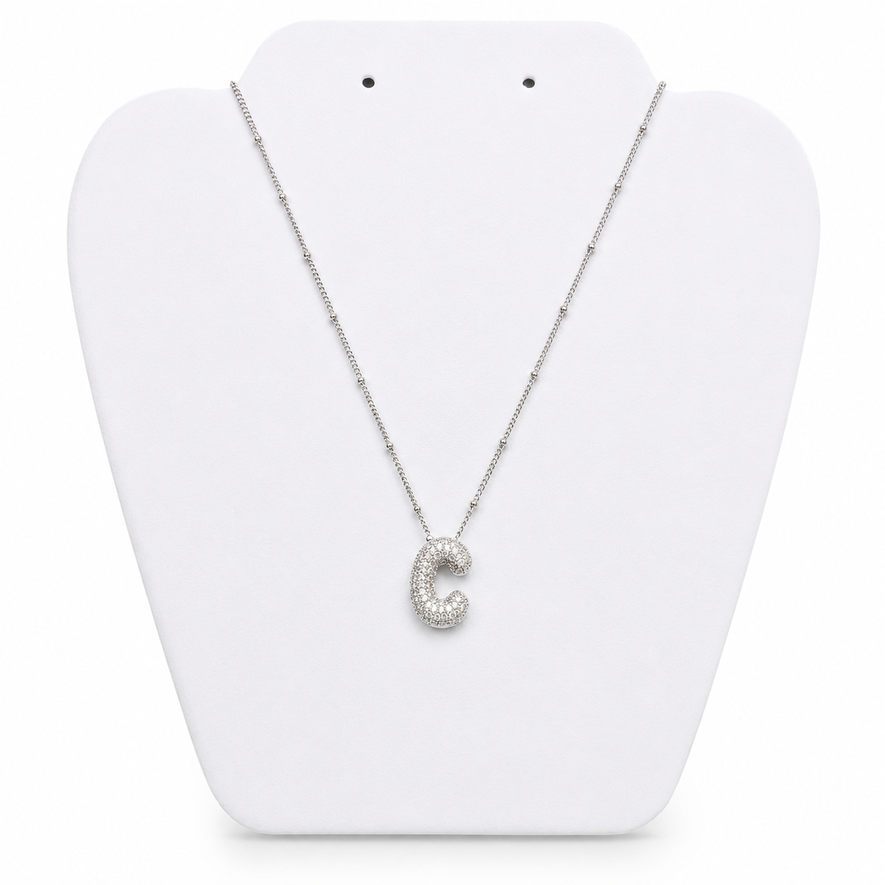 A silver initial necklace featuring the letter 'C' paved with small clear stones, displayed on a white plastic jewelry bust.