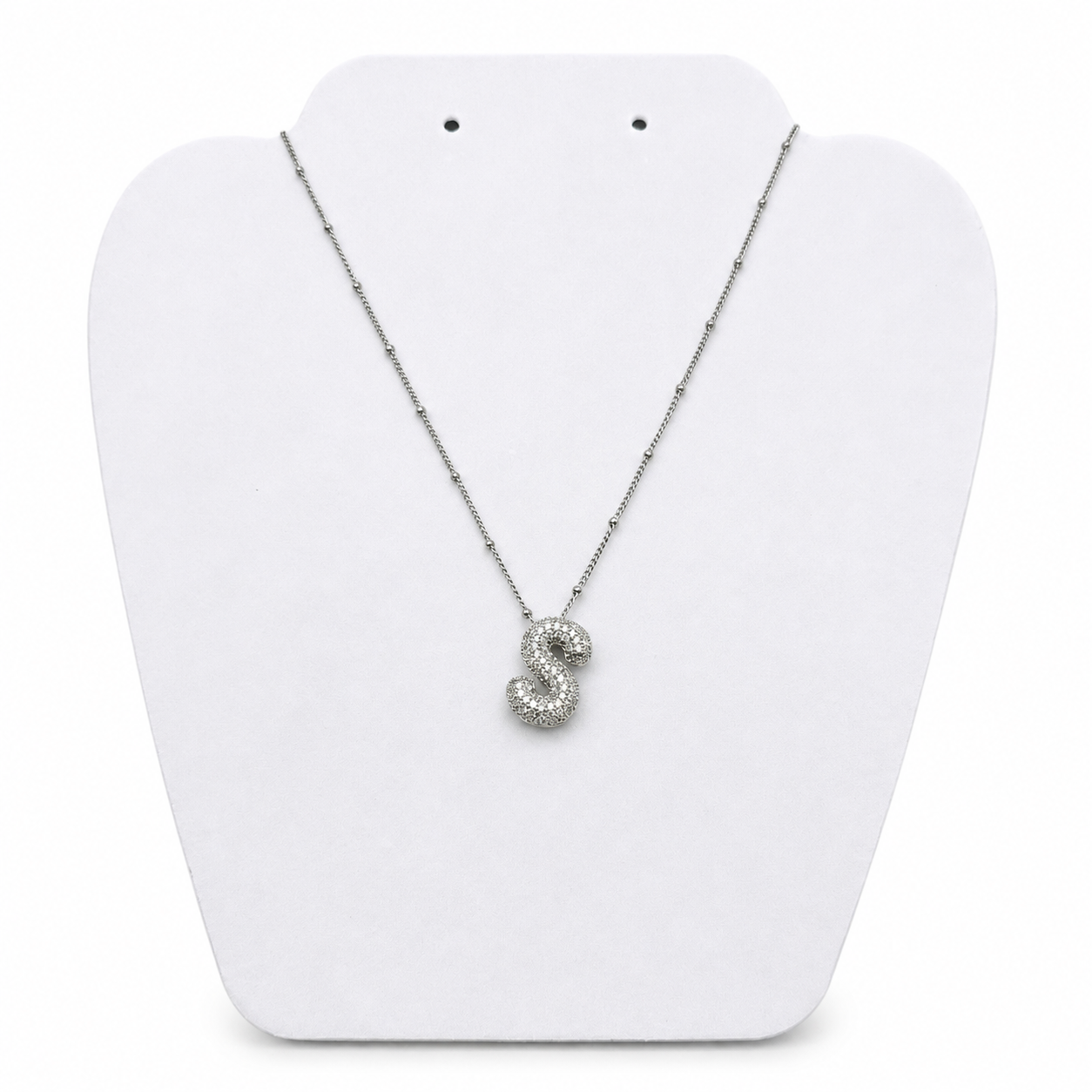 A silver necklace with a sparkling, textured pendant shaped like the letter 'S', displayed on a white plastic jewelry bust against a white background.