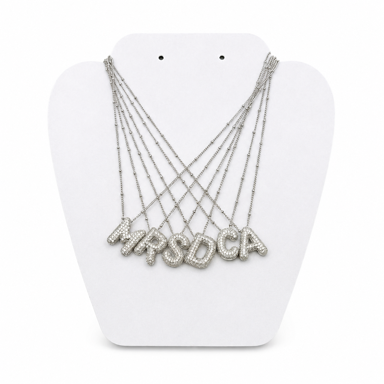 A multi-strand silver necklace with letter-shaped pendants spelling 'MPSDCA', displayed on a white neck stand against a white background.